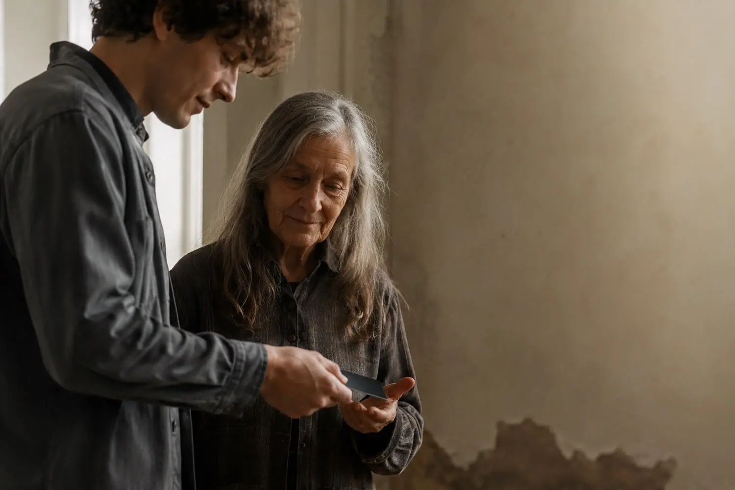 A younger member and an older woman by a window, the card passing between them.