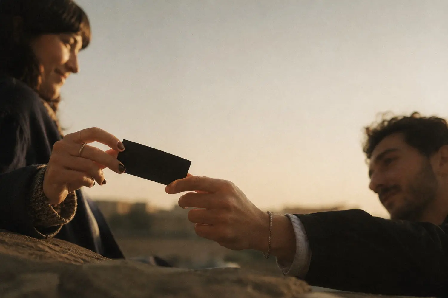 The card passing from one hand to another at dusk, on a hilltop above the coast.
