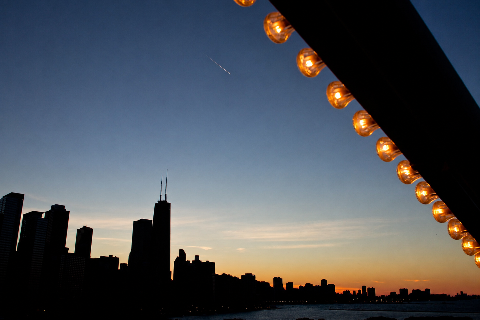 Chicago skyline at sunset beneath a row of illuminated Ferris wheel lights